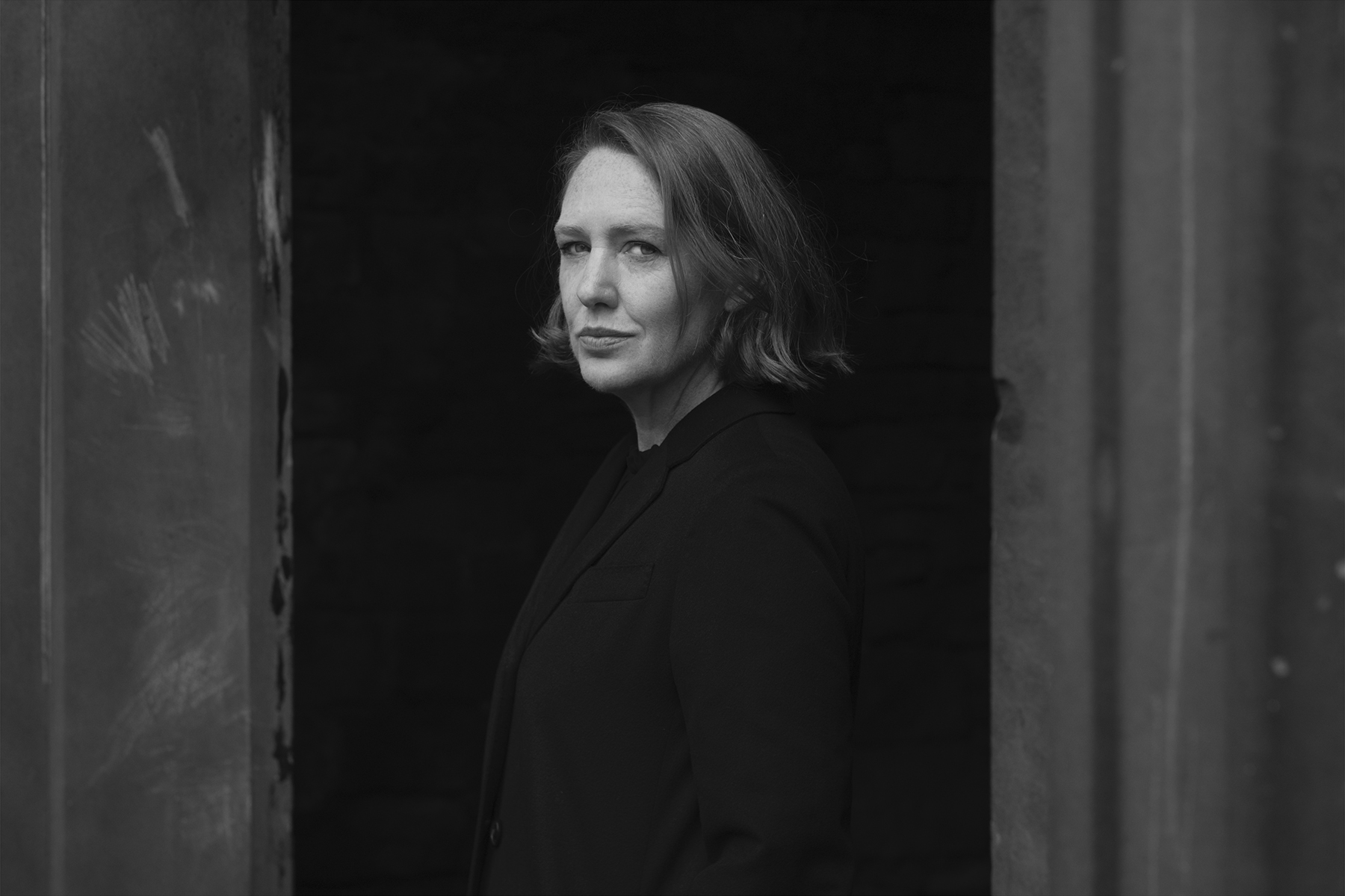 A black and white photo of Paula Hawkins' head and shoulders, as she looks directly towards the viewer.