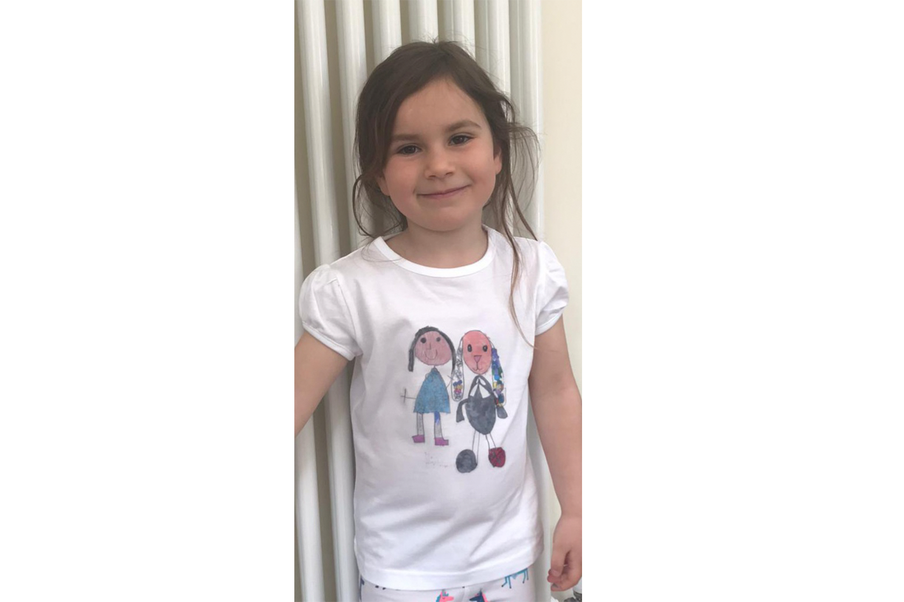 A young girl wearing a T-shirt with her drawing of herself and her cuddly toy on it