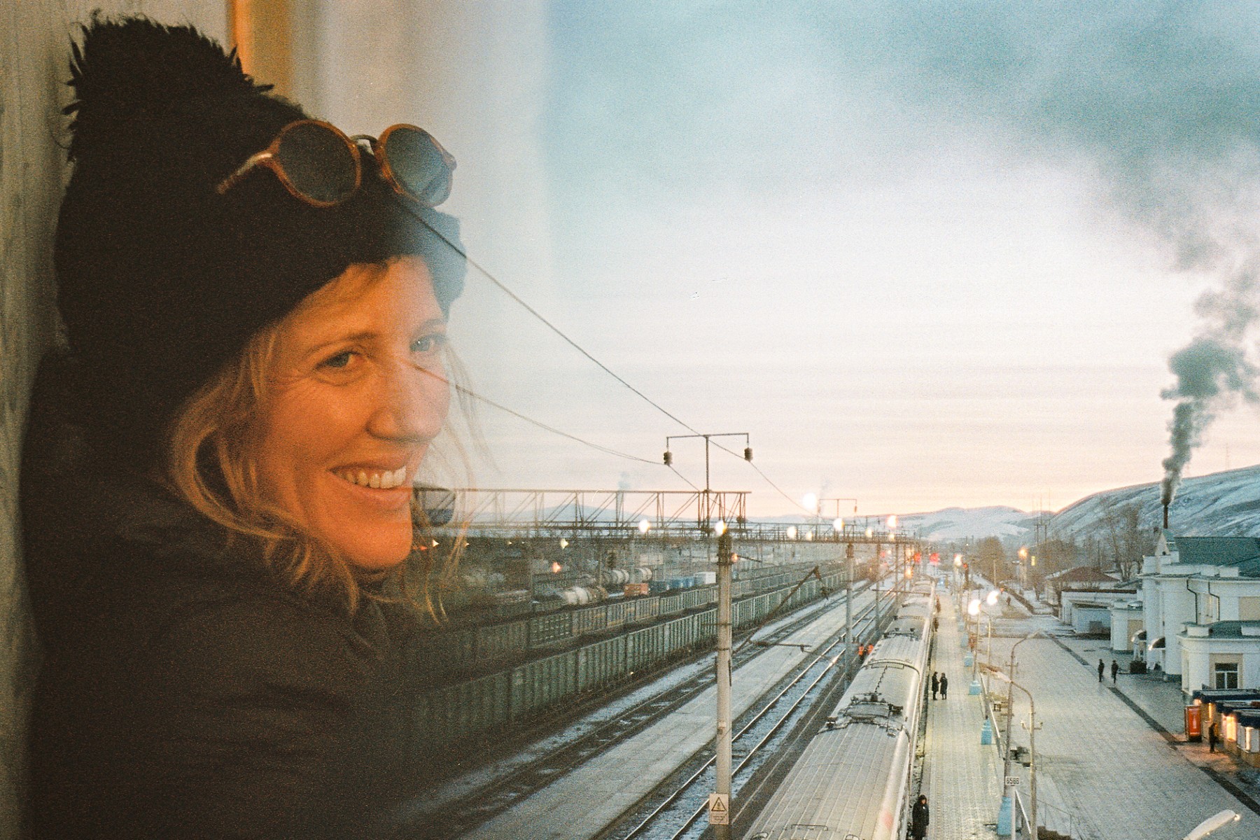 A photo of Sophy Roberts, author of The Lost Pianos of Siberia, with a rail station in the background.