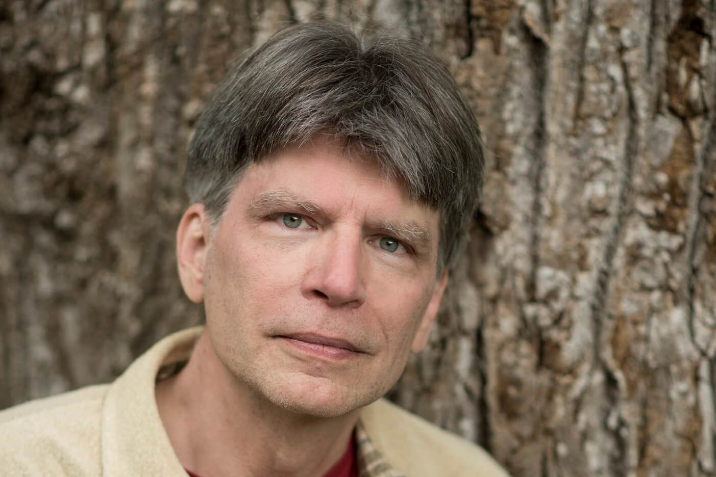 Richard Powers, photographed standing in front of a tree.