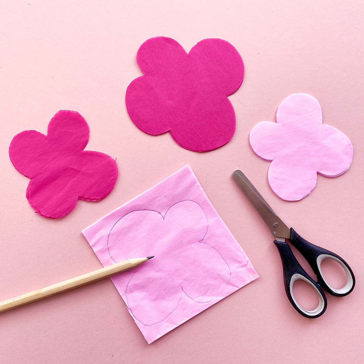 Photo of pink tissue paper with a simple flower design drawn on in pencil alongside some scissors, ready to cut out