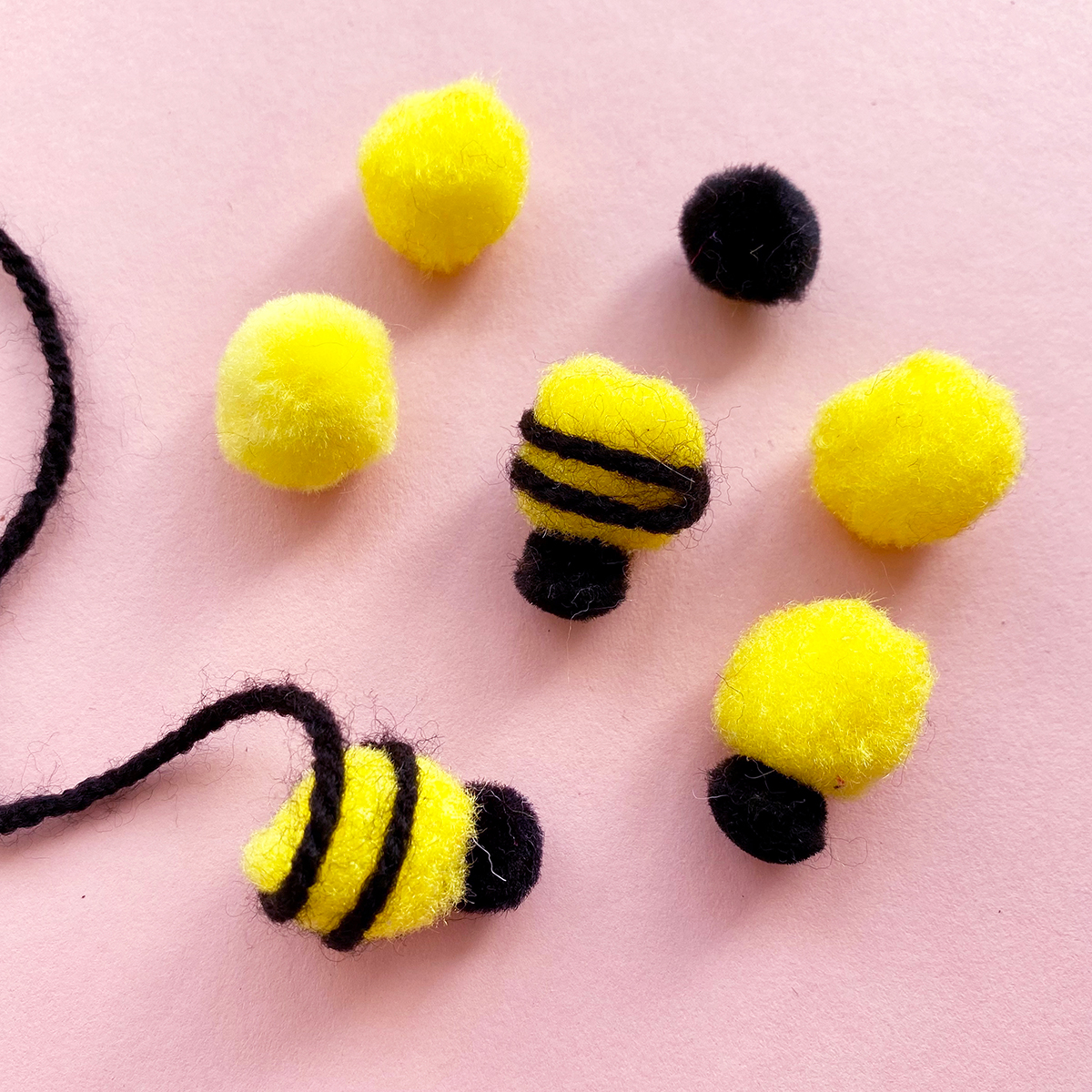 Photo of yellow pom poms being wrapped in black wool to resemble a bees body
