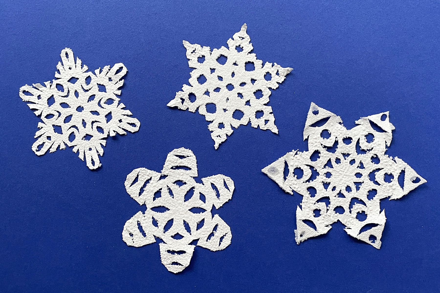 A photo of four paper snowflakes covered in salt crystals laid out next to each other on a dark blue table