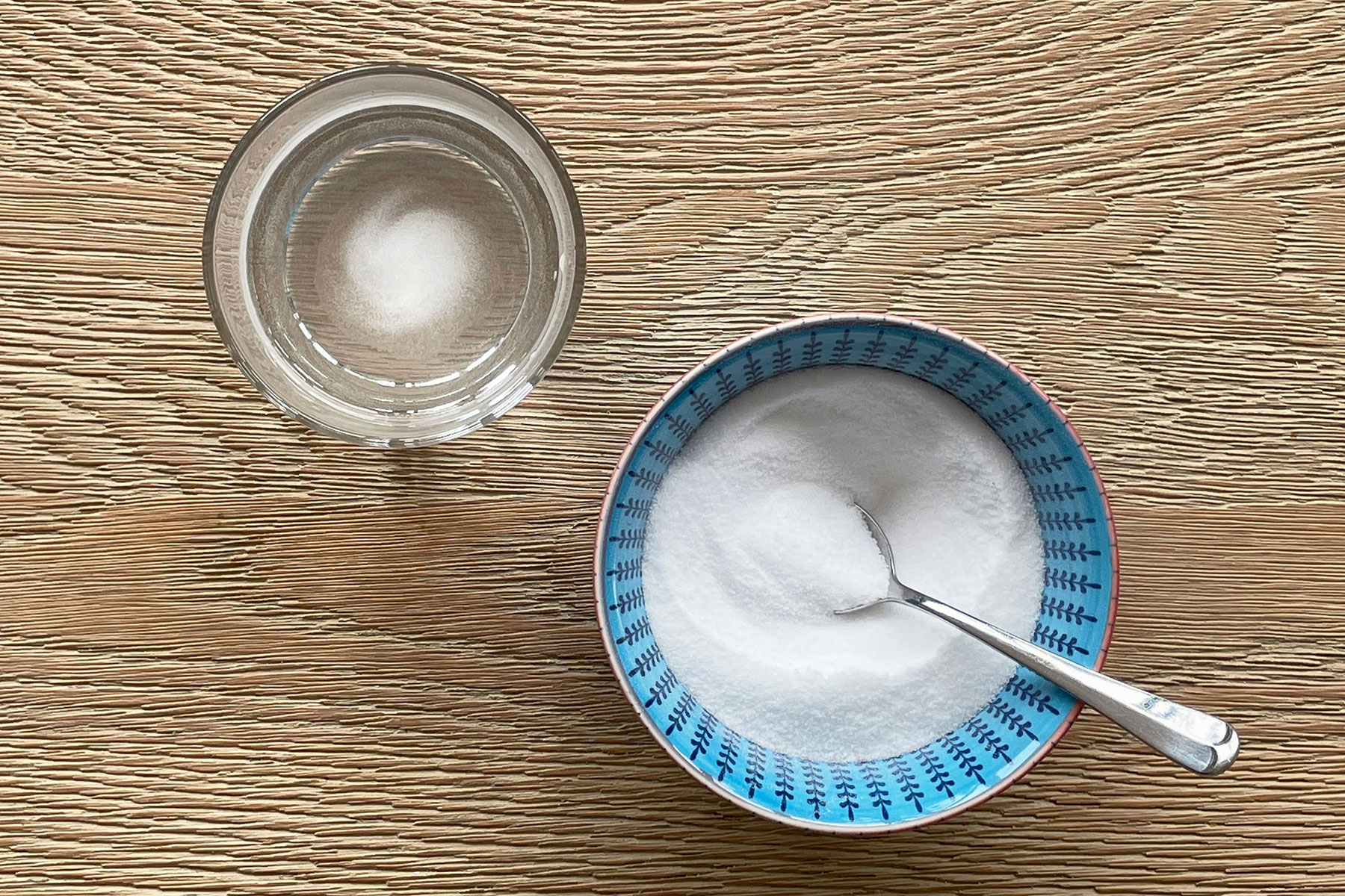 A photo of a bowl of salt with a spoon in it next to a cup of hot water